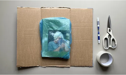 En kartong öppen med en bok inuti en plastpåse placerad på kartongen.