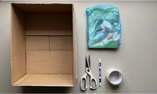 En kartong, sax, penna, tejp och en bok inuti en plastpåse.
